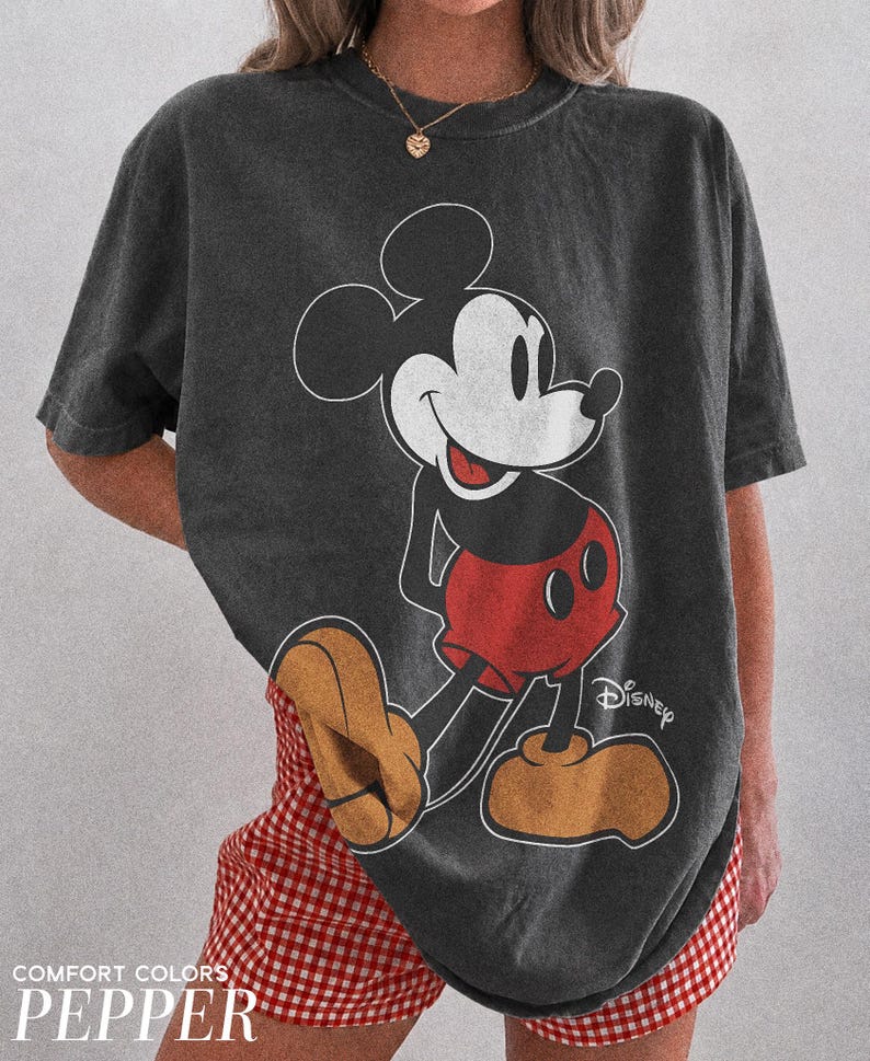 K&ouml;nnte beinhalten: Dunkelgraues T-Shirt mit einer Mickey Mouse-Grafik in Schwarz, Wei&szlig; und Rot. Auf dem T-Shirt ist das Wort "Disney" aufgedruckt. Der Text "COMFORT COLORS PEPPER" ist unten aufgedruckt. Teil der Comfort Colors-Kollektion.
