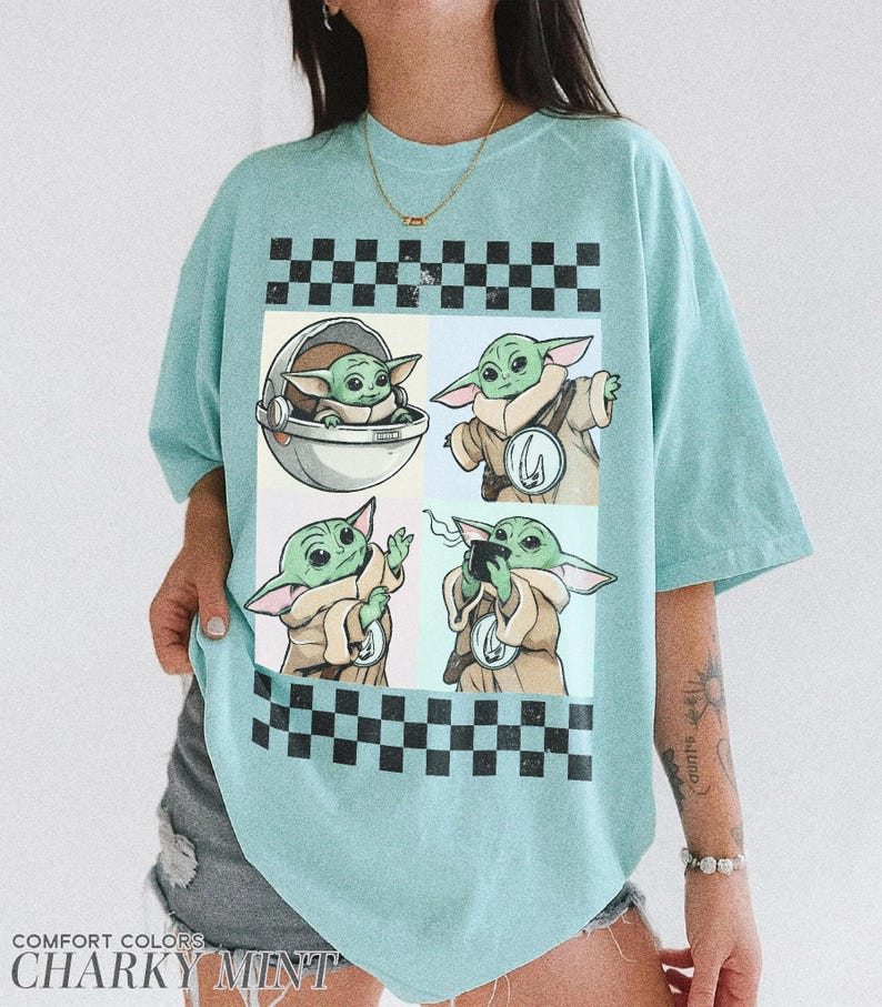 Puede incluir: Camiseta azul claro con un gr&aacute;fico de cuatro paneles de un personaje alien&iacute;gena verde. Los paneles est&aacute;n enmarcados por patrones de cuadros blancos y negros. La camiseta tiene las palabras "COMFORT COLORS" y "CHARKY MINT" impresas en la parte inferior.