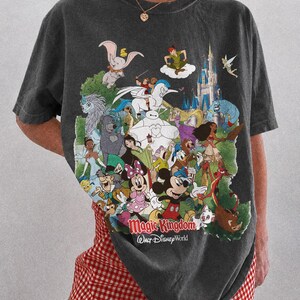 Peut inclure: T-shirt gris fonc&eacute; avec un imprim&eacute; color&eacute; de personnages Disney, dont Mickey et Dumbo. Le texte "Magic Kingdom Walt Disney World" est imprim&eacute;. Fait partie de la collection Comfort Colors Pepper.