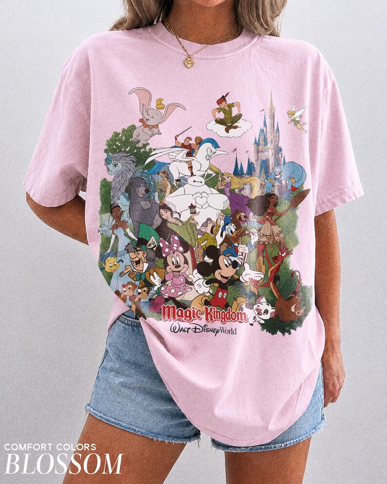 Peut inclure: T-shirt rose clair avec un imprim&eacute; color&eacute; de personnages Disney, dont Mickey, Minnie et Dumbo. Le texte "Magic Kingdom Walt Disney World" est imprim&eacute; en dessous. Le t-shirt est &eacute;tiquet&eacute; "Comfort Colors Blossom".