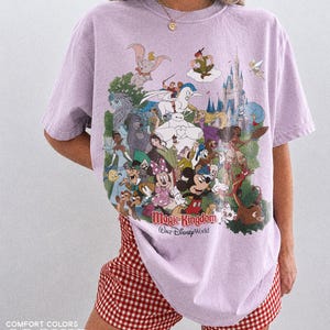 Peut inclure: Un t-shirt lilas avec un imprim&eacute; color&eacute; de personnages Disney, dont Mickey Mouse et Cendrillon. Les mots "Magic Kingdom Walt Disney World" sont imprim&eacute;s en dessous. Le t-shirt est port&eacute; avec un short &agrave; carreaux rouges et blancs.