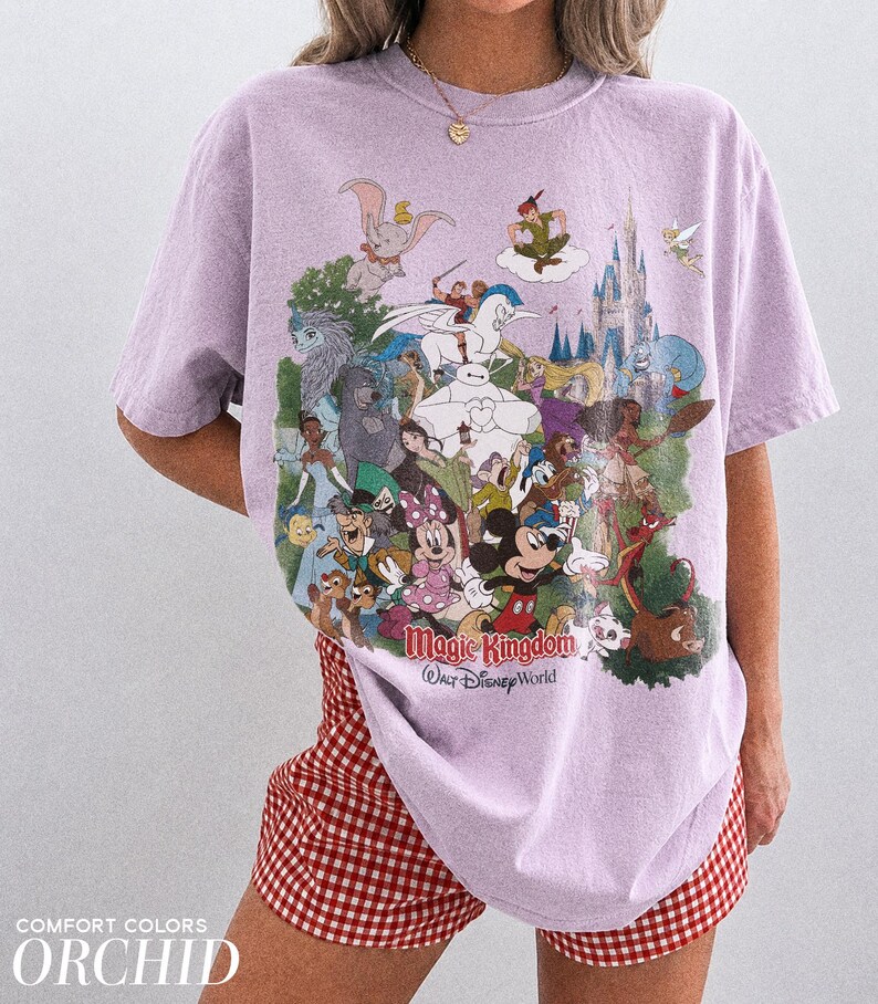 Peut inclure: Un t-shirt lilas avec un imprim&eacute; color&eacute; de personnages Disney, dont Mickey Mouse et Cendrillon. Les mots "Magic Kingdom Walt Disney World" sont imprim&eacute;s en dessous. Le t-shirt est port&eacute; avec un short &agrave; carreaux rouges et blancs.