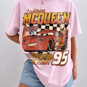 K&ouml;nnte beinhalten: Hellrosa T-Shirt mit einem Lightning McQueen-Motiv aus dem Film Cars. Das Design enth&auml;lt den Text "Lightning McQueen", "Cars", "95" und "Think Fast". Das Shirt ist ein Comfort Colors Blossom.