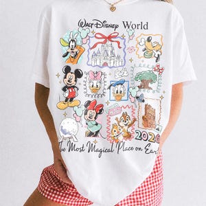 May include: White t-shirt featuring a colorful graphic of Walt Disney World characters and landmarks. The design includes Mickey Mouse, Goofy, and Cinderella's castle, with the text "Walt Disney World" and "The Most Magical Place on Earth."