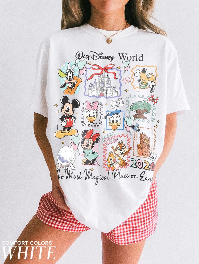May include: White t-shirt featuring a colorful graphic of Walt Disney World characters and landmarks. The design includes Mickey Mouse, Goofy, and Cinderella's castle, with the text "Walt Disney World" and "The Most Magical Place on Earth."