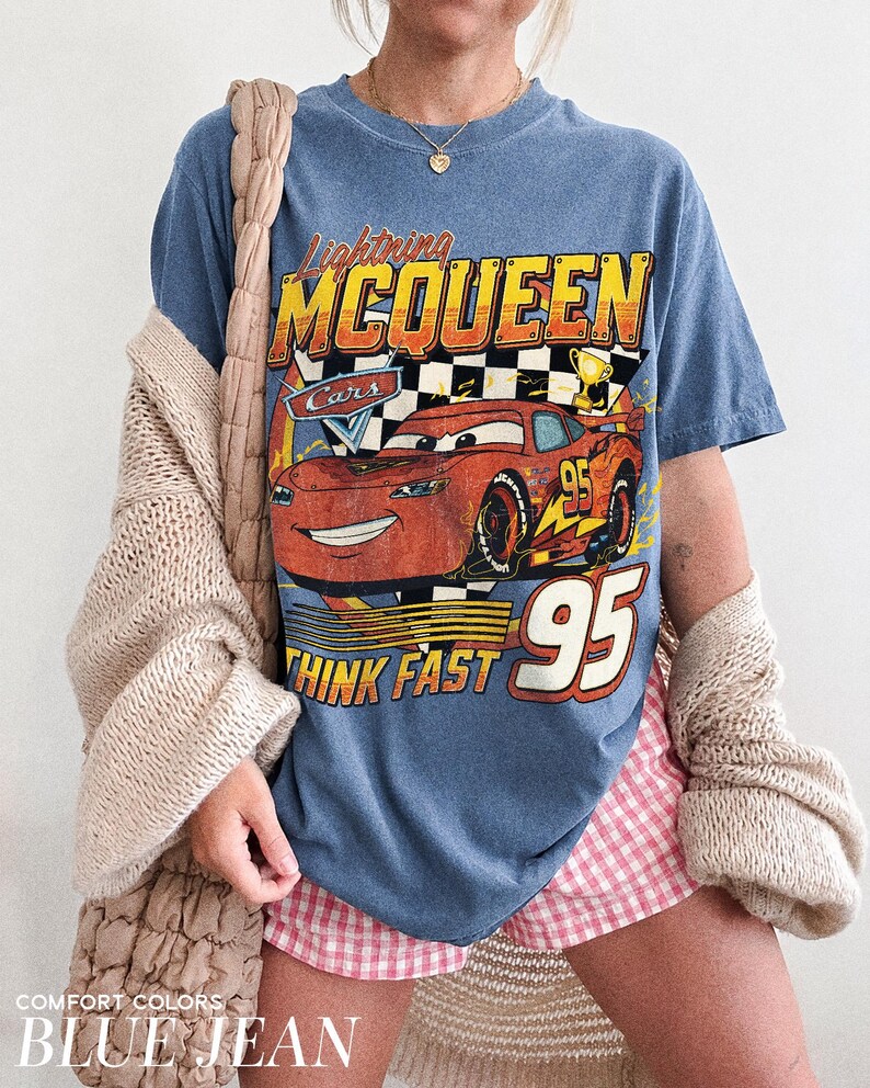 K&ouml;nnte beinhalten: Blaues Jeans-T-Shirt mit einem Aufdruck von Lightning McQueen aus dem Film Cars. Das Design enth&auml;lt den Text "Lightning McQueen", "Cars", "Think Fast" und die Nummer "95". Das Shirt ist eine Komfortfarbe.