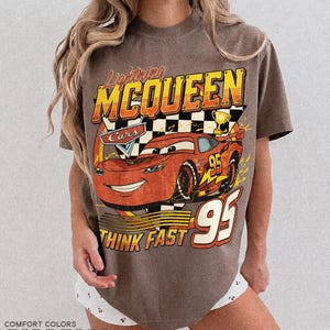 K&ouml;nnte beinhalten: Espressofarbenes T-Shirt mit einer Grafik von Lightning McQueen aus dem Film Cars. Das Design enth&auml;lt den Text "Lightning McQueen", "Cars", "95" und "Think Fast". Das Shirt hat einen Vintage-Look.