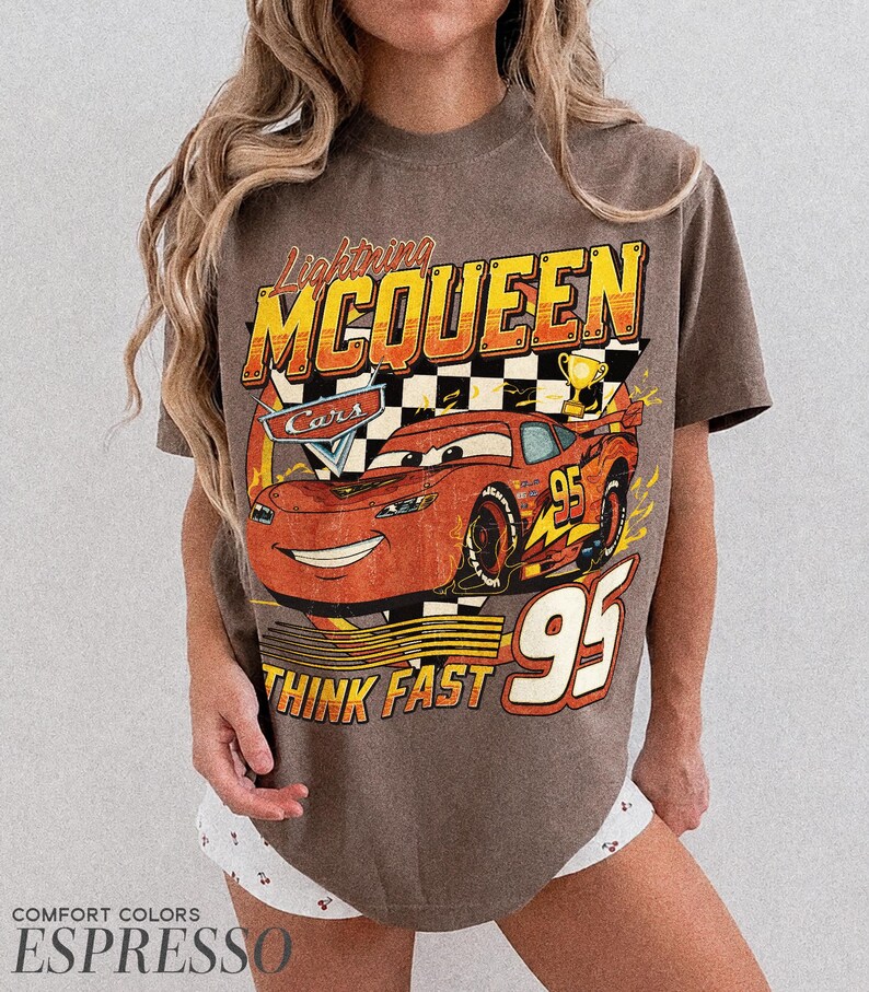 K&ouml;nnte beinhalten: Espressofarbenes T-Shirt mit einer Grafik von Lightning McQueen aus dem Film Cars. Das Design enth&auml;lt den Text "Lightning McQueen", "Cars", "95" und "Think Fast". Das Shirt hat einen Vintage-Look.