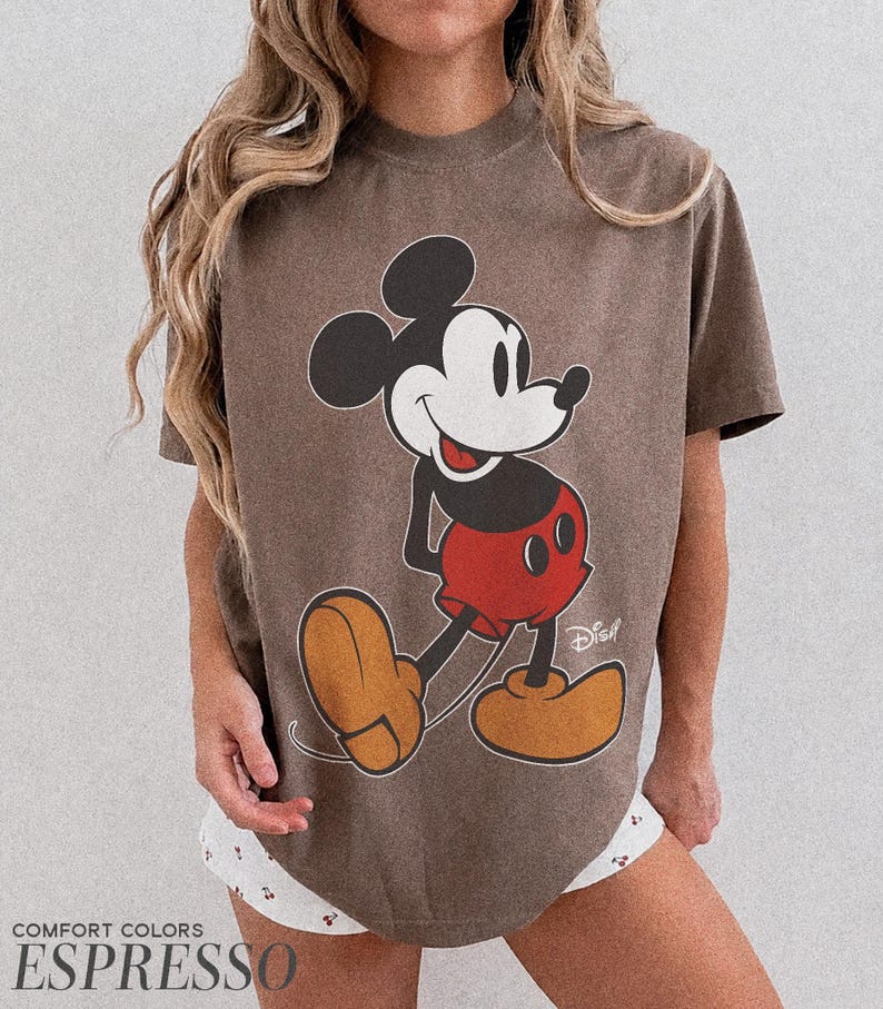 K&ouml;nnte beinhalten: Espressofarbenes T-Shirt mit einer gro&szlig;en Grafik von Mickey Mouse in seiner klassischen Pose. Die Zeichentrickfigur ist in Schwarz, Wei&szlig;, Rot und Beige dargestellt. Auf dem Shirt stehen die Worte "Comfort Colors" und "Espresso".