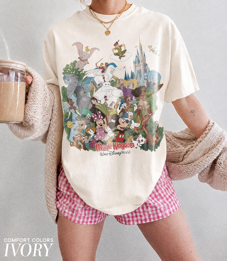 Peut inclure: T-shirt ivoire avec un graphisme color&eacute; de personnages Disney, dont Mickey Mouse et Peter Pan. Le mot "Magic Kingdom" est imprim&eacute; sur le t-shirt. Le short est &agrave; carreaux roses et blancs.