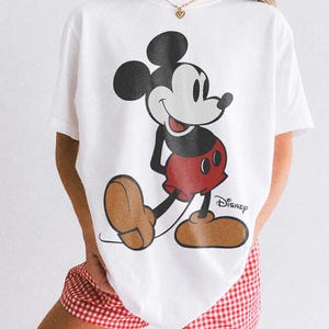 K&ouml;nnte beinhalten: Wei&szlig;es T-Shirt mit einer Mickey Mouse-Grafik in Schwarz, Rot und Braun. Das Disney-Logo ist auf dem T-Shirt aufgedruckt. Der Text "COMFORT COLORS WHITE" ist unten im Bild aufgedruckt.