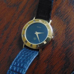Ladies black dial Gucci, Swiss, gold plate bezel with Roman Numerals and strap 3000L
