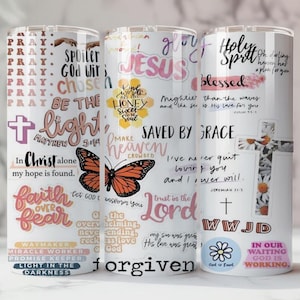 May include: Three stainless steel tumblers with a white background, covered in inspirational text and graphics. The designs include phrases like "Saved by Grace," a butterfly, and crosses. The tumblers are designed for cold beverages.