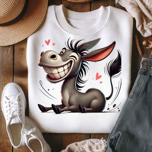 Op de afbeelding: Wit sweatshirt met een cartoon ezel met een grote grijns. De ezel is grijs met zwarte accenten en rode hartdetails. Het sweatshirt wordt gecombineerd met witte sneakers en denim.