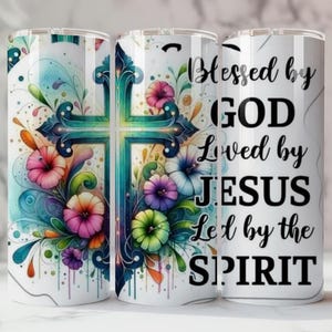 May include: A white tumbler with a teal cross design and colourful flowers. The tumbler has the text "Blessed by GOD Loved by JESUS Led by the SPIRIT" in black script. The design is in a watercolour style.