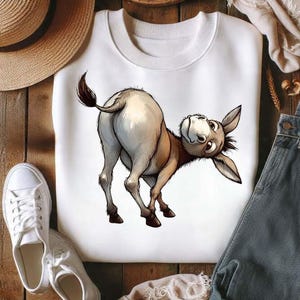 Op de afbeelding: Witte crewneck sweatshirt met een cartoon illustratie van een ezel. De ezel is van achteren afgebeeld, over zijn schouder kijkend. Het kunstwerk is gedetailleerd met bruine en bruinachtige tinten.