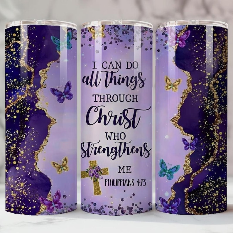 May include: A purple and gold tumbler with a design featuring butterflies and the text "I CAN DO all THINGS THROUGH CHRIST who STRENGTHENS ME Philippians 4:13." The tumbler has a gold and purple abstract design.