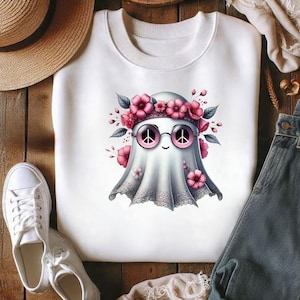 Pode incluir: Uma camisola branca de gola redonda com um gr&aacute;fico central de um fantasma a usar &oacute;culos de sol redondos com lentes cor-de-rosa em forma de sinal de paz e uma coroa de flores cor-de-rosa e folhas verdes.