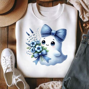 Pode incluir: Uma camisola branca de gola redonda com o gr&aacute;fico de um pequeno fantasma azul-claro com olhos grandes e escuros e bochechas rosadas. O fantasma usa um grande la&ccedil;o azul na cabe&ccedil;a e segura um ramo de flores azuis atado com uma fita azul.