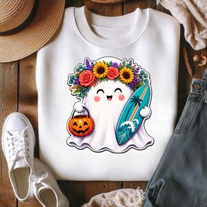 Pode incluir: Uma camisola branca de gola redonda com o gr&aacute;fico de um fantasma sorridente a usar uma coroa de flores coloridas de girass&oacute;is e rosas. O fantasma segura um balde de ab&oacute;bora laranja e uma prancha de surf turquesa com uma palmeira.