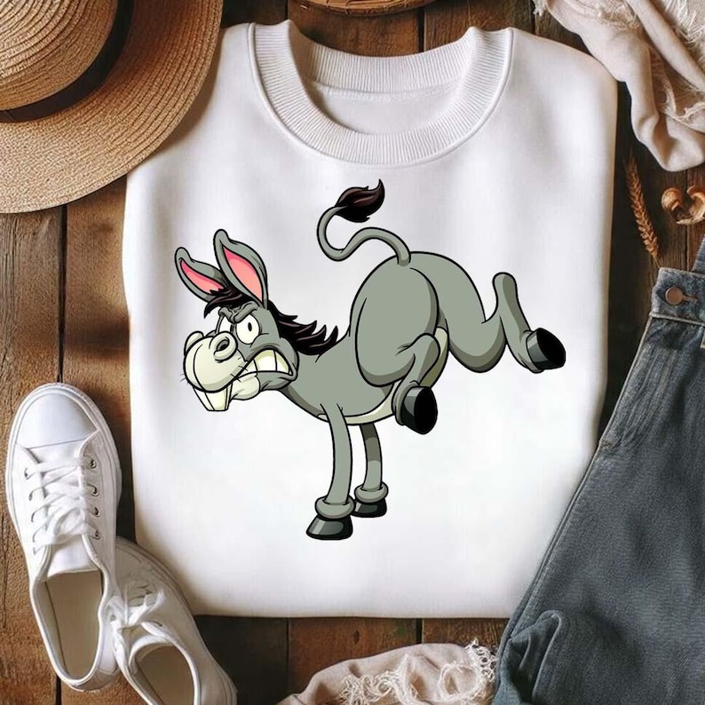Op de afbeelding: Witte sweatshirt met een cartoon ezel. De ezel is grijs met zwarte hoeven, een donkere manen en roze gevoerde oren. De ezel heeft een boze uitdrukking. De sweatshirt heeft een ronde hals.