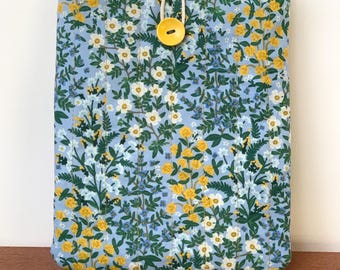 May include: A blue floral-patterned tablet sleeve with a yellow button closure. The sleeve features a repeating pattern of yellow and white flowers with green leaves on a light blue background. The button is attached with a white cord.