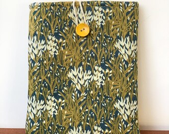 May include: A rectangular fabric case with a botanical pattern in shades of olive green, navy blue, and cream. The case is secured with a yellow button and a cream-colored string loop. The case is likely designed to hold a tablet or e-reader.