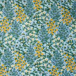 以下が含まれることがあります： 水色の生地に花柄。デザインは、黄、白、青の花と緑の葉のクラスターが特徴です。花は密集して配置され、鮮やかで詳細なパターンを作り出しています。
