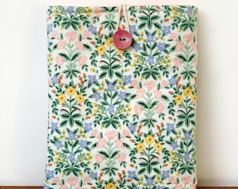 May include: A floral pattern tablet sleeve with a pink button closure. The fabric features a white background with a repeating pattern of pink, yellow, and blue flowers with green leaves. The button is a light pink color.