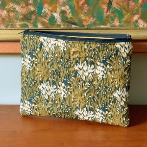 May include: A rectangular zipped pouch with a botanical pattern. The fabric has a dark teal background with a repeating design of white and gold-coloured plant-like shapes. The zip is dark teal with a gold-coloured pull.