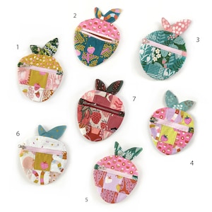 May include: Seven handmade strawberry-shaped coin purses. Each purse has a patchwork design with various fabrics, colours, and patterns, including floral and fruit motifs. They have a zip closure and green leaf accents.