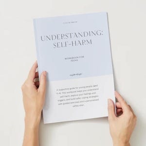 May include: A light blue and white workbook titled "UNDERSTANDING: SELF-HARM WORKBOOK FOR TEENS" is held by two hands. The book's cover features the title in a sans-serif font. The workbook is a supportive guide for young people aged 11-16.