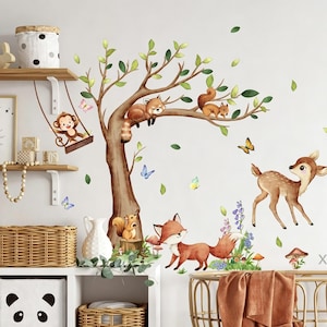 Könnte beinhalten: Ein Wandaufkleber-Set mit einem großen braunen Baum mit grünen Blättern, einem Affen auf einer Schaukel, einem roten Panda, einem Eichhörnchen, einem Fuchs und einem Reh. Das Design umfasst bunte Schmetterlinge, kleine Pilze und Blätter.