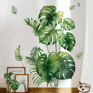 May include: Green and white tropical plant wall decals. The decals feature large monstera leaves and smaller palm fronds. The image also includes framed artwork with the text "EVERYTHING GOES WELL IN".