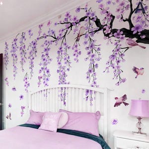 May include: A bedroom scene featuring a white headboard, a bed with pink bedding, and a wall adorned with a floral mural. The mural depicts a tree with purple flowers and birds, creating a serene and decorative ambiance.