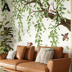 Könnte beinhalten: Ein braunes Ledersofa mit Zierkissen steht unter einem Wandbild mit einem Baum mit grünen Blättern und kleinen Vögeln. Der Buchstabe "A" ist in der oberen linken Ecke zu sehen.