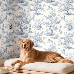 May include: A golden retriever rests on a cream-colored rectangular dog bed placed on a wooden platform. The wall behind features wallpaper with a blue and white toile pattern depicting trees and dogs. A small woven basket and bowl are nearby.