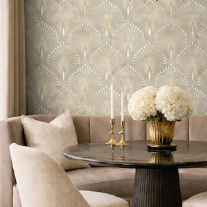 Op de afbeelding: Een ronde zwarte marmeren tafel met een gouden gecanneleerde voet, bekroond met een gouden vaas met witte hortensia's en twee gouden kandelaars. De achtergrond toont behang met een herhalend goud waaiermotief op een grijs gestructureerd oppervlak.