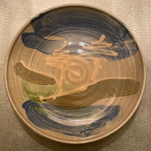 May include: A brown ceramic plate with a blue, green, and tan abstract design. The plate has a hand-painted look and a unique, artistic style.