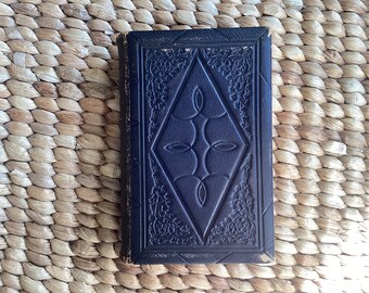May include: A black leather-bound book with an intricate embossed design on the cover. The design features a diamond shape with a floral pattern around the edges.