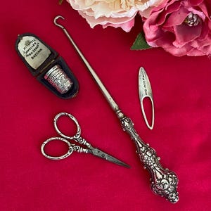 May include: A silver sewing set including a button hook with an ornate handle, a pair of small scissors, a thimble in a velvet-lined case marked J. MITCHELL JEWELLER HIGH STREET BRECHIN, and a small metal tool with engraved hallmarks.