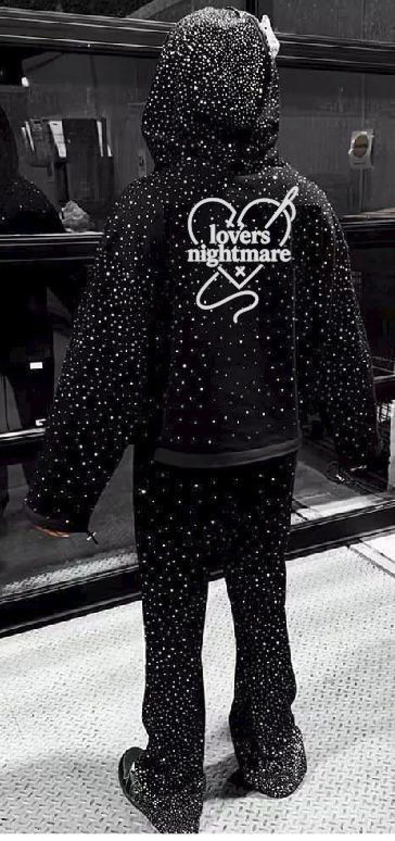 K&ouml;nnte beinhalten: Schwarzes Kapuzensweatshirt und passende Hose, beide mit funkelnden Verzierungen bedeckt. Auf der R&uuml;ckseite des Hoodies steht in Wei&szlig; der Text "lovers nightmare". Ein einzigartiges, auff&auml;lliges Ensemble.