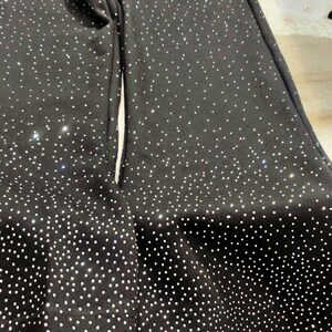 K&ouml;nnte beinhalten: Schwarze Jogginghose mit wei&szlig;em Punktmuster und Kordelzug in der Taille. Die Hose hat ein wei&szlig;es Logo auf dem oberen linken Bein. Der untere Saum der Hose ist ebenfalls mit wei&szlig;en Punkten bedeckt. Die Hose ist aus einem weichen, bequemen Material.