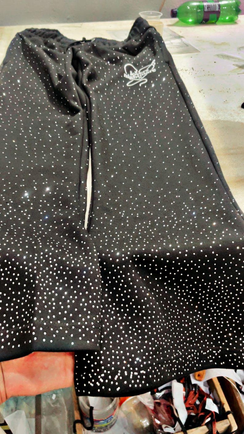K&ouml;nnte beinhalten: Schwarze Jogginghose mit wei&szlig;em Punktmuster und Kordelzug in der Taille. Die Hose hat ein wei&szlig;es Logo auf dem oberen linken Bein. Der untere Saum der Hose ist ebenfalls mit wei&szlig;en Punkten bedeckt. Die Hose ist aus einem weichen, bequemen Material.