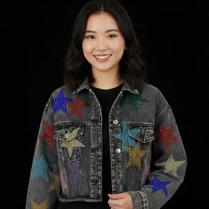 May include: A cropped denim jacket in a dark gray wash, embellished with colorful rhinestone star appliqués. The jacket features a classic button-up design with pockets and the word "Goldiver" in gold lettering.