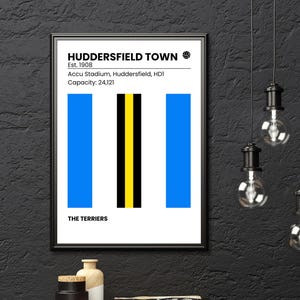 Könnte beinhalten: Gerahmtes Poster mit dem Logo des Fußballvereins Huddersfield Town. Das Design umfasst blaue und gelbe vertikale Streifen auf weißem Hintergrund. Der Text oben lautet "HUDDERSFIELD TOWN" und "Est. 1908". Der Text unten lautet "THE TERRIERS".