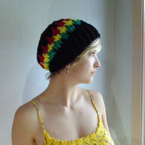 Może przedstawiać: Czarna czapka z szydełka z czerwonymi, żółtymi i zielonymi paskami. Czapka jest ręcznie robiona i ma prążkowaną fakturę. Stylowy dodatek do noszenia na co dzień.
