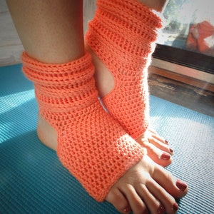 May include: A pair of coral-colored crochet toe socks with an open heel design. The socks are worn on a person's feet and are resting on a blue yoga mat.