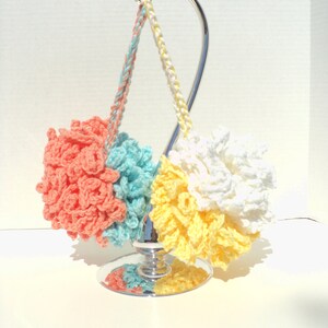 May include: Three crocheted pom-poms in coral, turquoise, and yellow hanging on a silver stand.