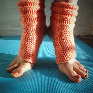 May include: A pair of coral-colored crocheted ankle warmers on a blue yoga mat.